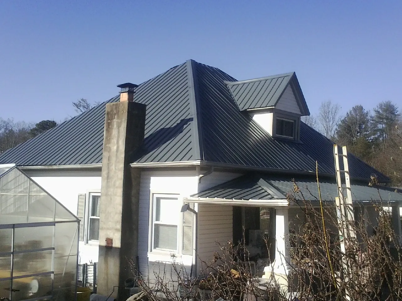 Dark blue standing seam metal roof on a white farmhouse with dormer — Slate & Tile Roof Repair by Roofing Brothers in East Ryegate