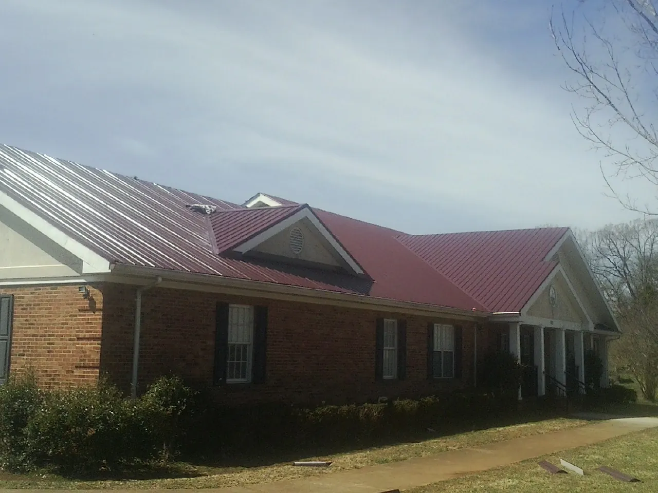 Red metal roof with gabled entries on a long brick building, from a Hail Damage Roof Repair job in East Ryegate