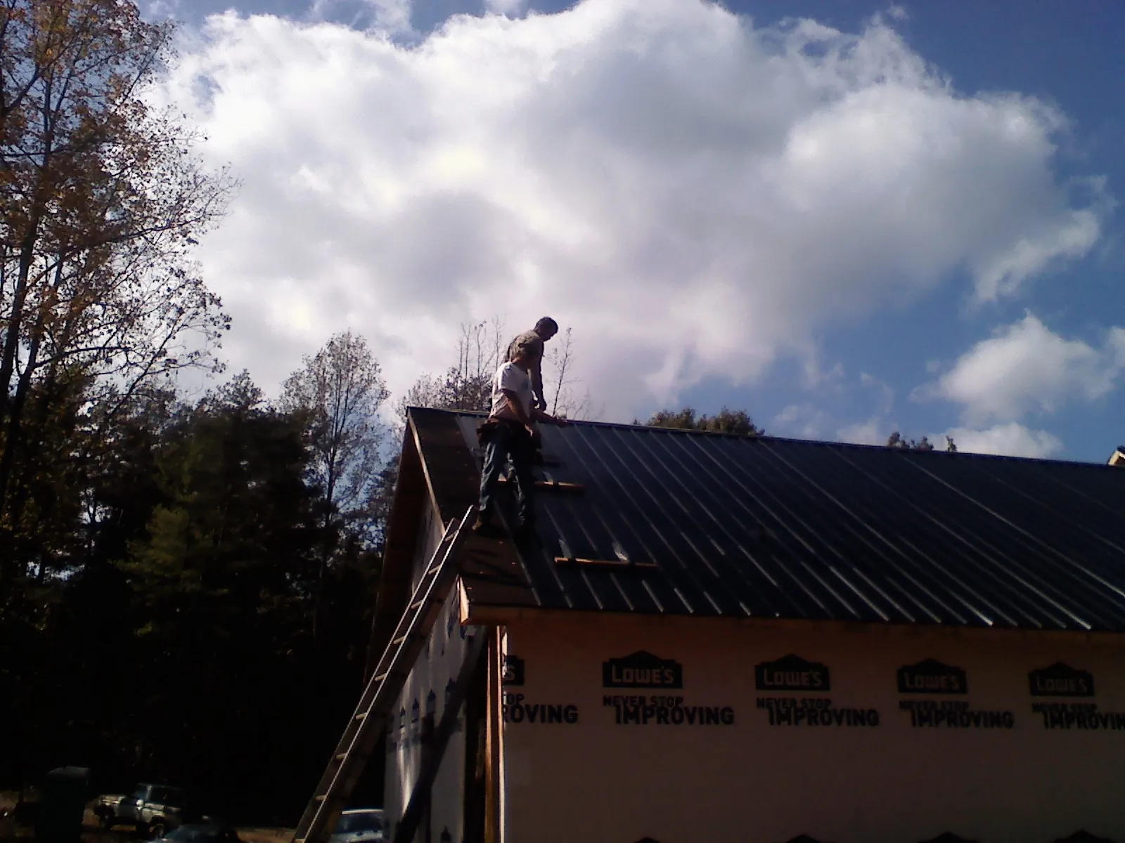 Roofer fastening dark metal panels high against a cloudy sky, from a Roof Inspection job in East Ryegate