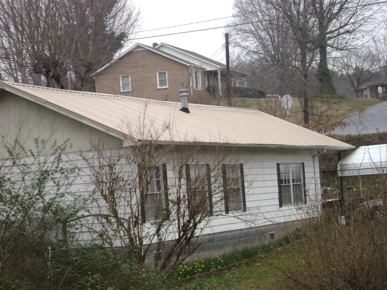 Tan metal roof on a white sided house set into a hillside — Commercial Roofing by Roofing Brothers in East Ryegate