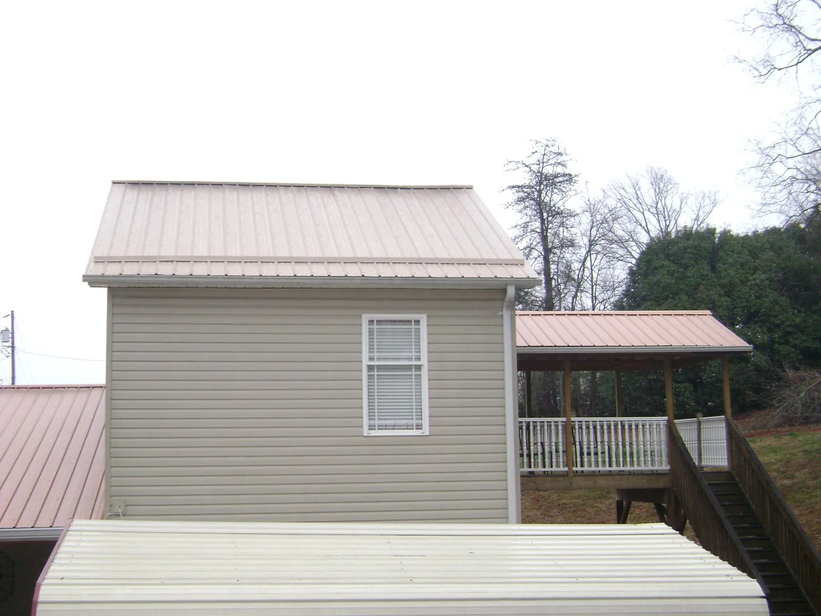 Tan metal roofs on a two story addition and attached porch, from a Roof Replacement job in East Ryegate